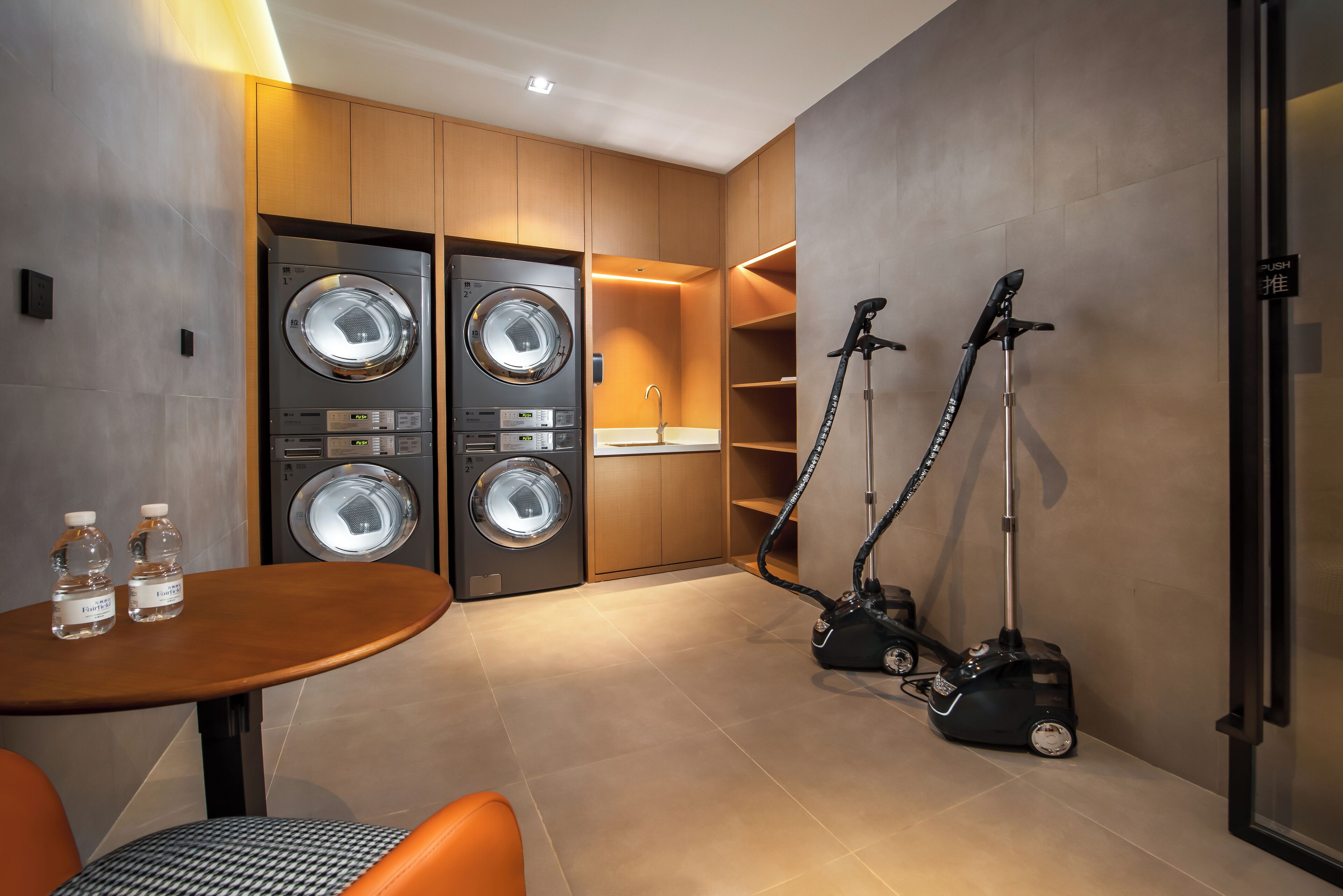 A compact laundry area with two front-loading washing machines, a sink, and two vacuum cleaners.