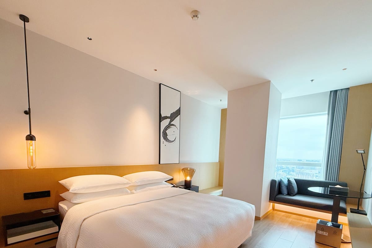 Moderni hotellihuone, jossa on suuri sänky, näköala kaupunkiin, sohva ja työpöytä.