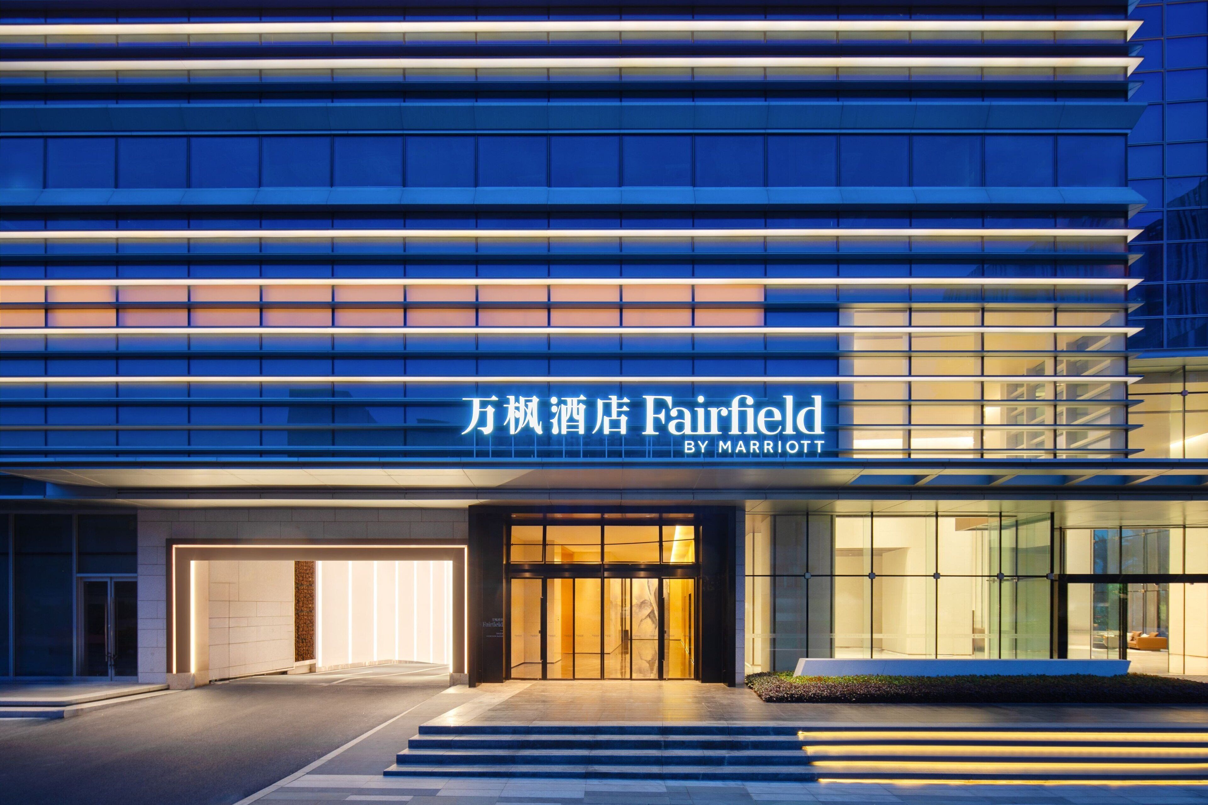 Fachada moderna de hotel con letreros iluminados, entrada de cristal y zona de acceso bien iluminada.