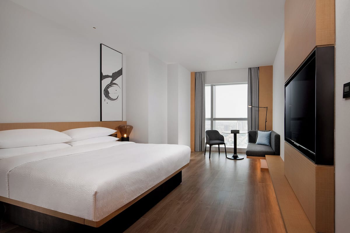 Moderni hotellihuone, jossa on suuri sänky, taulutelevisio, pieni pöytä ja tuoli.