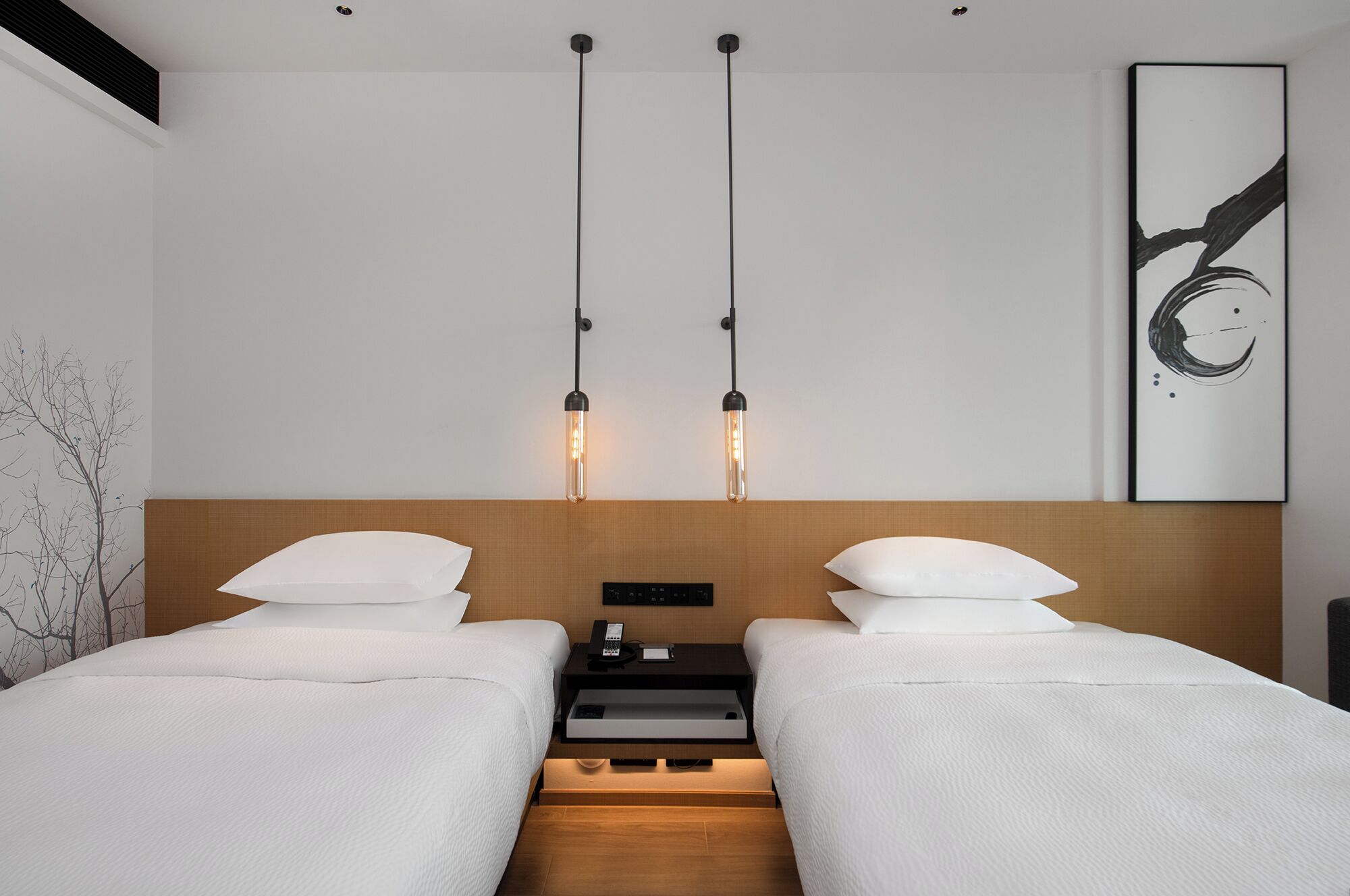 A modern hotel room with two beds, a wooden headboard, a nightstand with a phone, and a wall-mounted artwork.