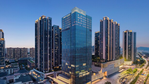 Un moderno grattacielo con facciata in vetro, circondato da altri edifici di grandi dimensioni, e una strada trafficata con veicoli.