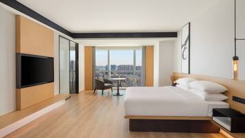 Una habitación de hotel moderna con una cama grande, un televisor de pantalla plana, vistas a la ciudad y una pequeña mesa con una silla.