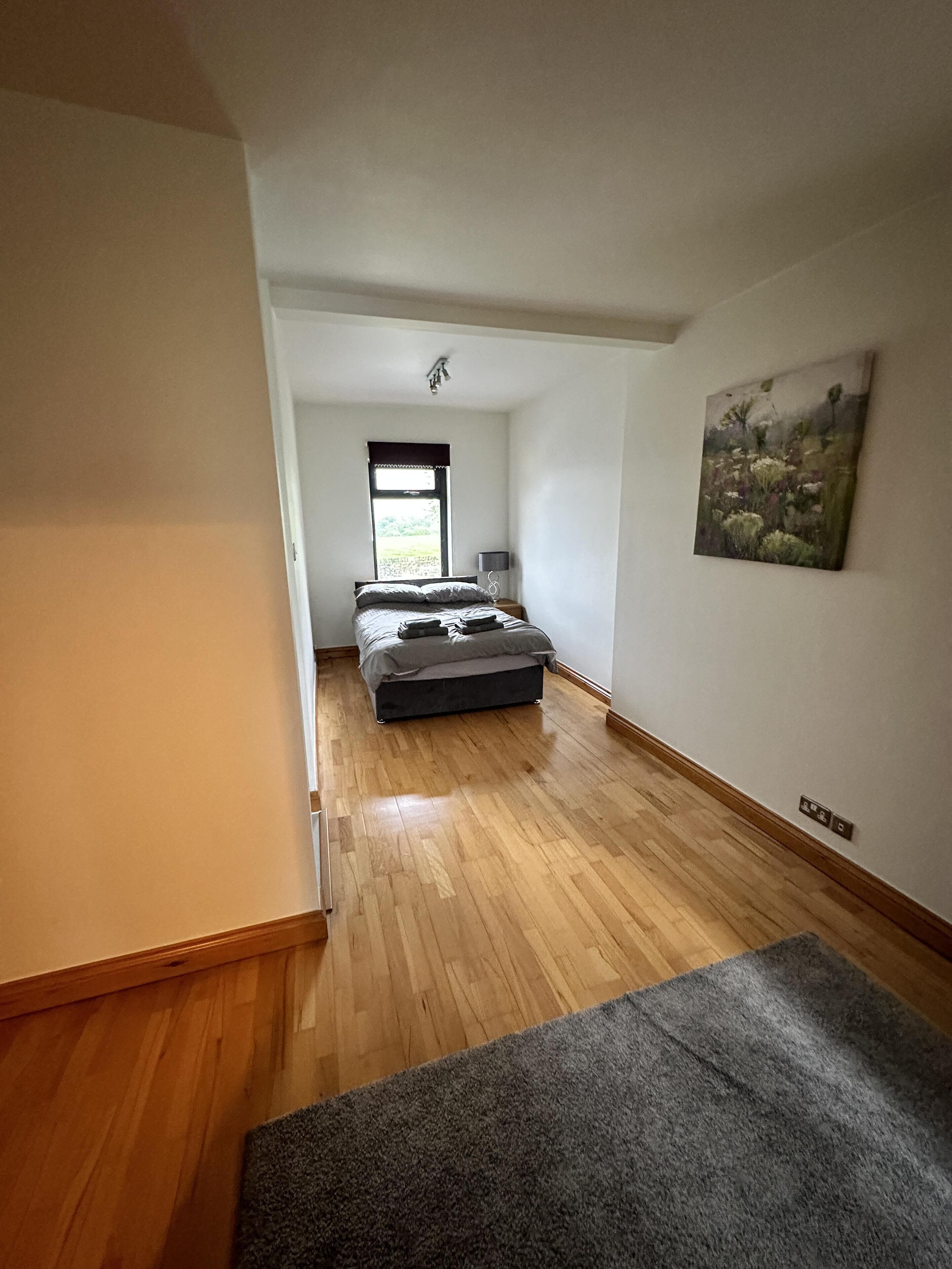 A bedroom with a bed, a window, a painting, and a carpet.