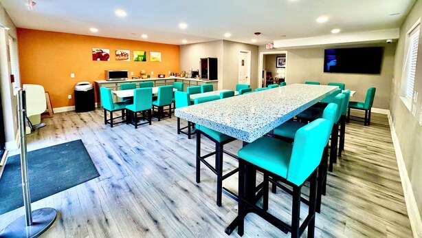 Una cocina moderna con una isla grande, un comedor con sillas color turquesa y un televisor de pantalla plana montado en la pared.