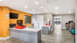 Un área de recepción con mostrador, un televisor de pantalla plana, un extintor y una puerta que da a otra habitación.