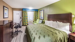 Una habitación de hotel con cama, escritorio, silla y cómoda.
