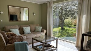 Ein Wohnzimmer mit einer Couch, einem Glastisch und Blick auf einen Garten durch eine Schiebetür.