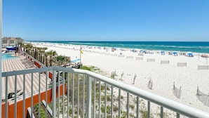 Blick auf einen Strand vom Balkon aus, mit Pool, Sonnenschirmen und Liegestühlen.