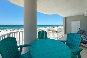 Un balcon avec vue sur la plage, une porte blanche, ainsi que des chaises et une table de couleur turquoise.