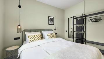 Ein ordentlich eingerichtetes Hotelzimmer mit Bett, einer Pendelleuchte, einem gerahmten Bild an der Wand und einem eingebauten Kleiderschrank mit Kleiderstange.