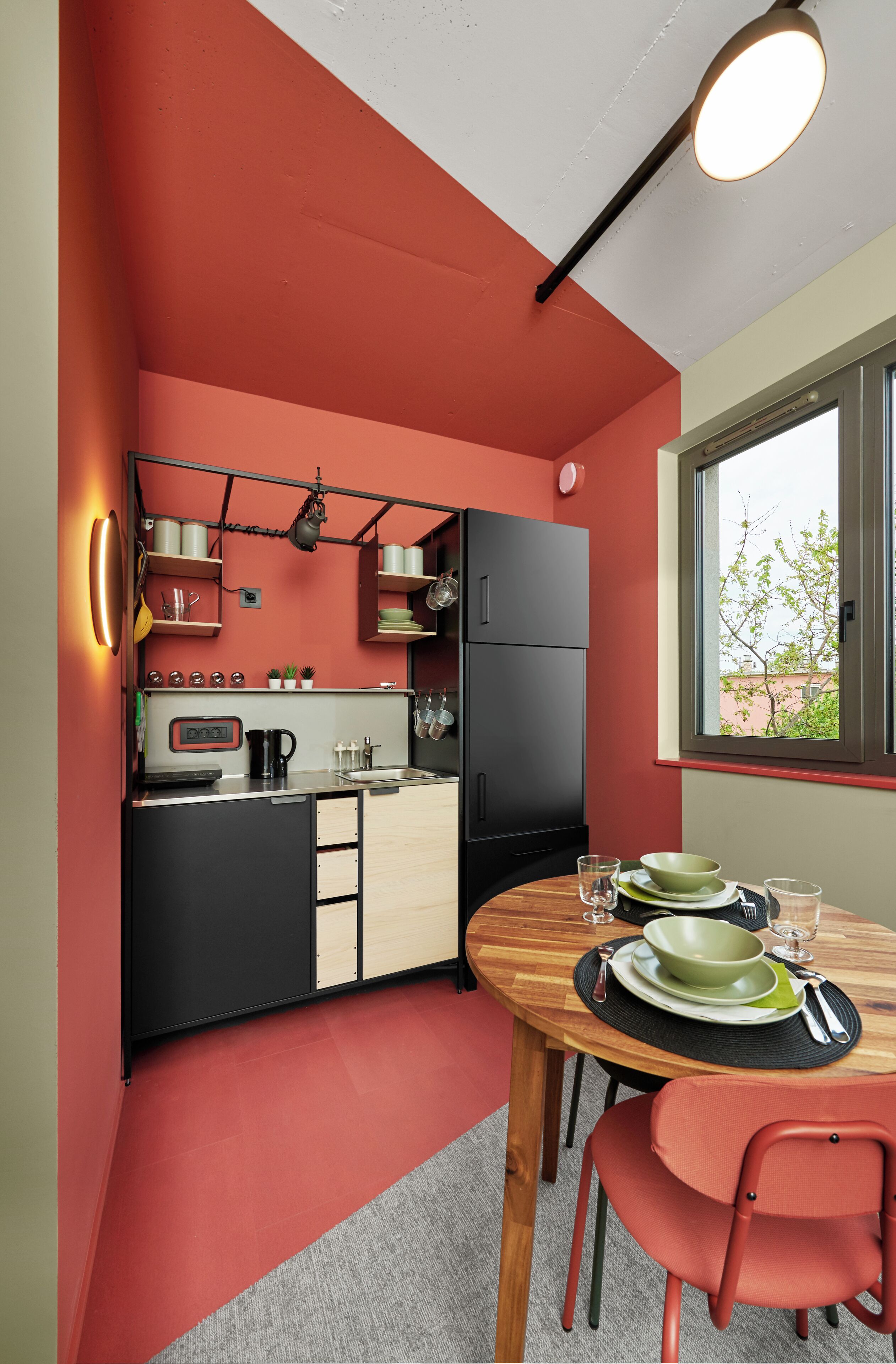 A compact kitchen with a red wall, black cabinets, and a wooden dining table with chairs.