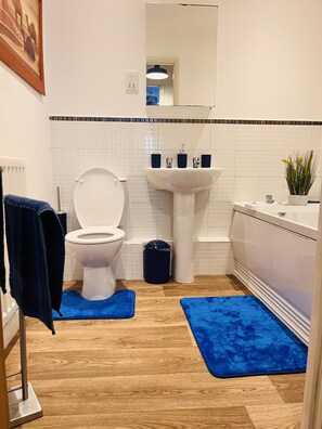 A bathroom with a toilet, sink, mirror, and blue mats on the floor. - Beautiful 2 - Bed Apartment in Aylesbury (Aylesbury)