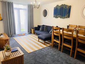 A modern living room with a sofa, wooden chairs, a striped rug, and a wall art piece. - Beautiful 2 - Bed Apartment in Aylesbury (Aylesbury)