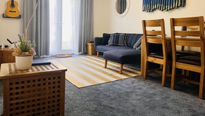 Ein Wohnzimmer mit einer Couch, Sesseln, einem Teppich, einer Zimmerpflanze, einer Gitarre und einem Wandbild.