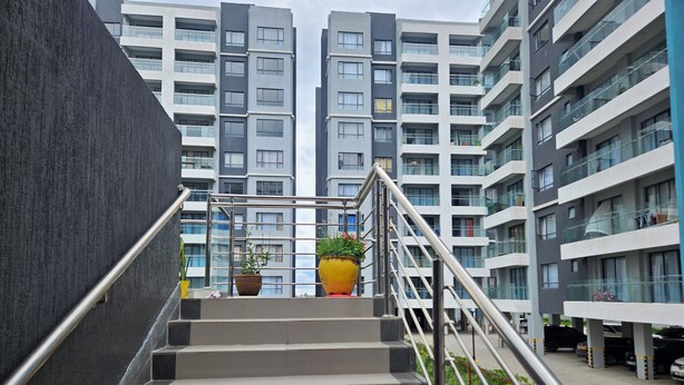 A staircase leading to a modern apartment building with multiple floors, metal railings, and potted plants on the landing. - Apt 5 - 1BR Apartment with a pool, high-speed internet, close to the airport (Nairobi)
