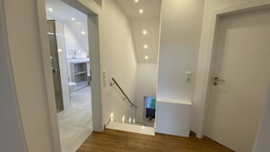 A modern interior with a wooden floor, a staircase, and a door leading to another room.