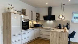 A modern kitchen with white cabinets, a built-in oven, a microwave, and a coffee machine.