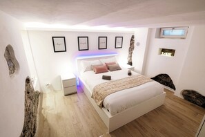 A modern bedroom with a large bed, framed artwork on the wall, and a unique rock feature on the left wall. - Lake Como Love (Como)