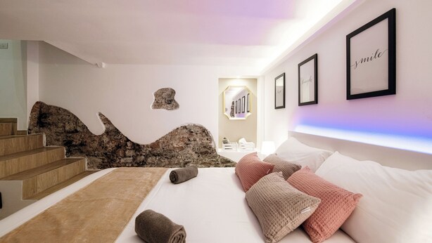 A bedroom with a bed, pillows, a rug, and a stone wall. - Lake Como Love (Como)