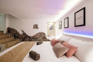 Un dormitorio con cama, almohadas, una alfombra y una pared de piedra.