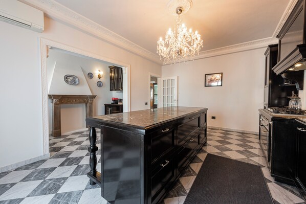 A spacious kitchen with a large island, black cabinetry, a chandelier, and a checkered floor.