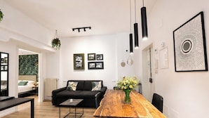 A modern living room with a wooden dining table, black chairs, a black sofa, and a coffee table. There are framed pictures on the wall, a hanging plant, and a large abstract artwork. - Casa Foresta - Apartment in Sorrento Centre (Sant'Agnello di Sorrento)