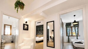 A modern hotel room with a white armchair, a bed with a headboard, a mirror, and a dining area with a table and chairs. - Casa Foresta - Apartment in Sorrento Centre (Sant'Agnello di Sorrento)