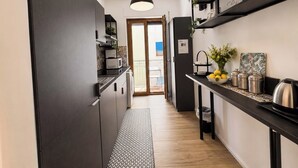 A narrow kitchen with dark cabinetry, a hanging pendant light, and a small dining area with a table and chairs. - Casa Foresta - Apartment in Sorrento Centre (Sant'Agnello di Sorrento)