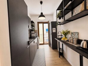 A narrow kitchen with dark cabinetry, a hanging pendant light, and a small dining area with a table and chairs.