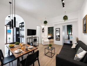 Un espace de vie moderne comprenant un coin repas, un canapé, un téléviseur et une cuisine visible à travers une arche.