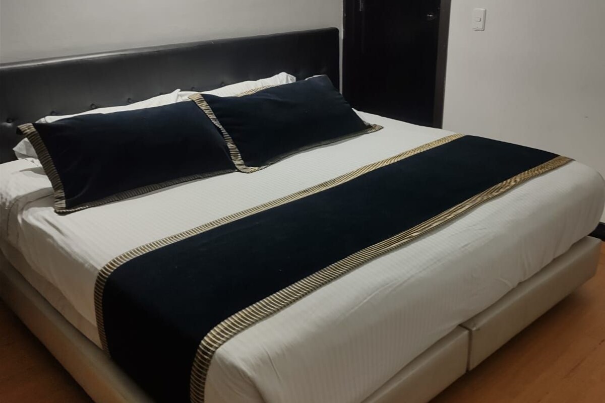 Una cama con cabecera, una mesita de noche y una puerta en una habitación con suelo de madera.