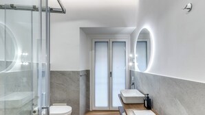 Un baño moderno con cabina de ducha de vidrio, lavabo blanco y tocador de madera.