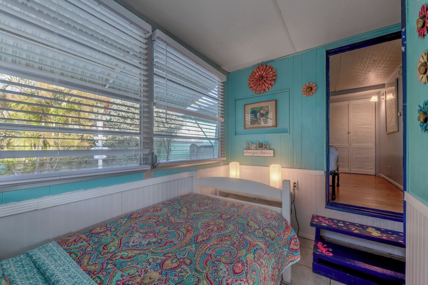 A bedroom with a bed, a window with blinds, a door, and a wall with a picture and a sign.