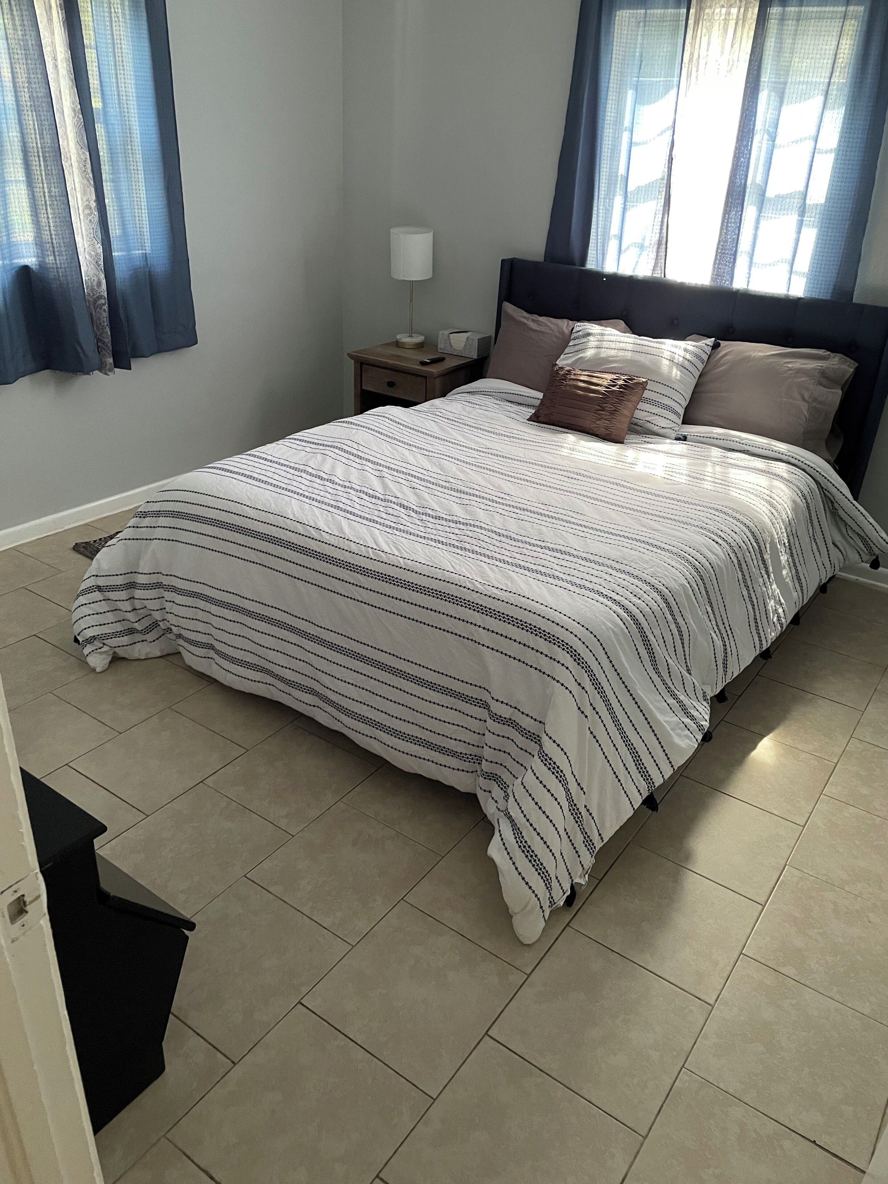 A neatly made bed with a striped bedspread, a bedside lamp, and a nightstand with a tissue box and remote control.