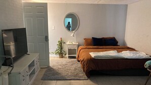 Ein Schlafzimmer mit Bett, Fernseher, Spiegel, Nachttisch und einer Topfpflanze.