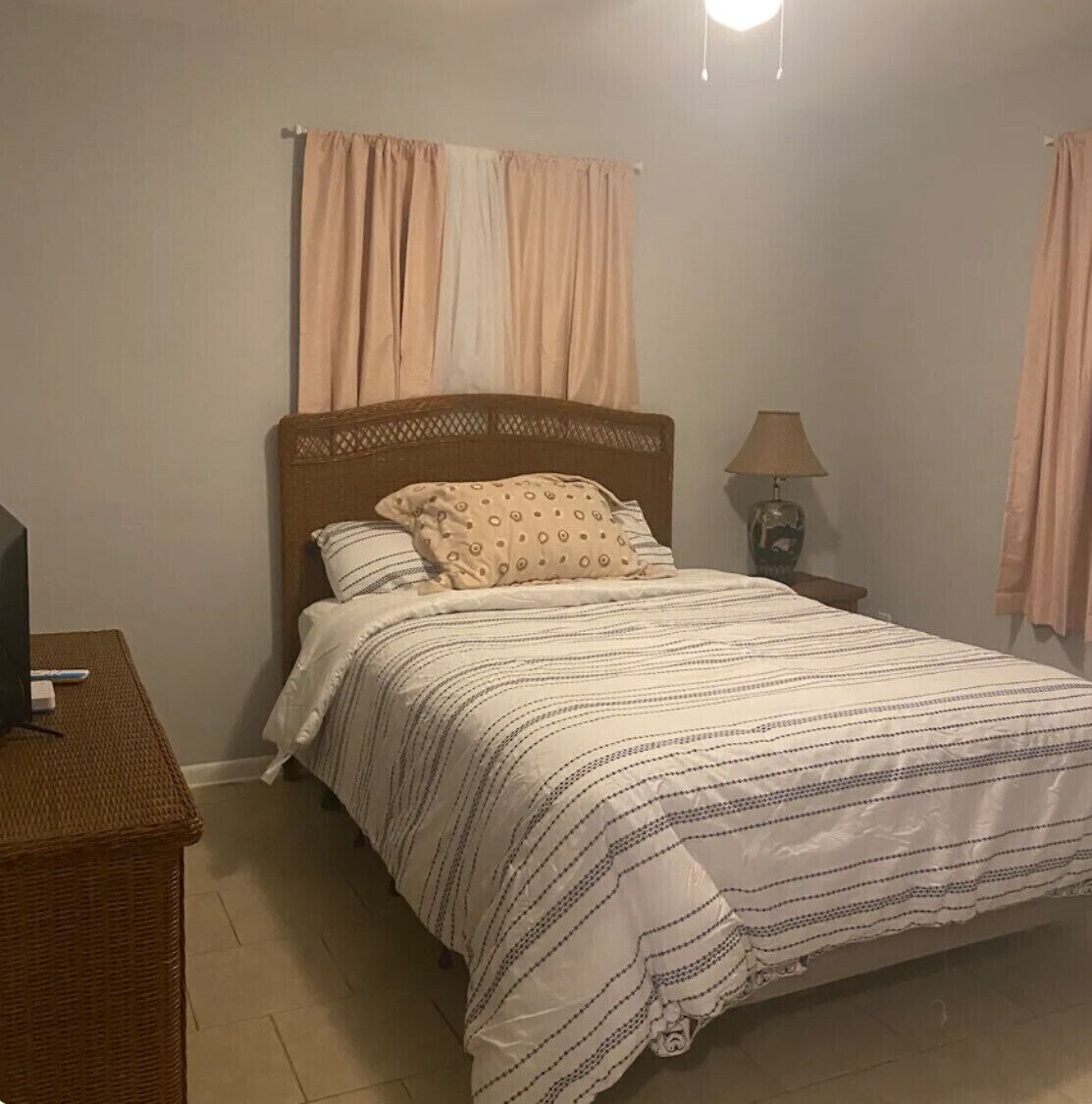 Un letto rifatto con lenzuola a righe, una testiera, una lampada da comodino e un televisore su un tavolino accanto al letto.