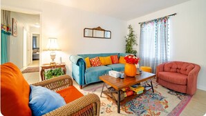 Ein Wohnzimmer mit einem blauen Sofa, orange- und blauem Kissen und einem hölzernen Couchtisch sowie einem roten Sessel.