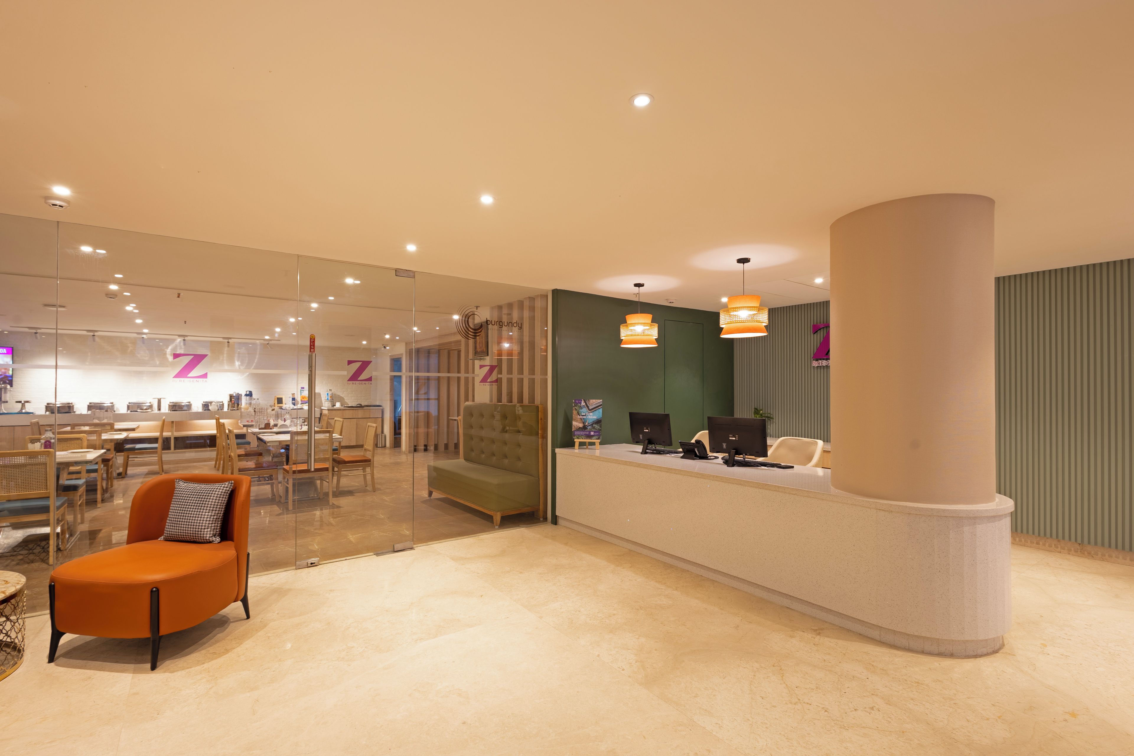 A modern hotel lobby with a reception desk, seating area, and a glass partition.
