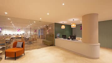 A modern hotel lobby with a reception desk, seating area, and a glass partition.