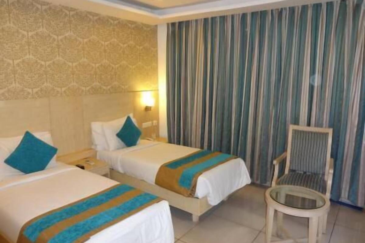 A hotel room with two beds, a nightstand, a chair, and a curtain.