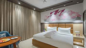 A hotel room with a bed, a desk with a chair, a wall with a floral mural, and a window.
