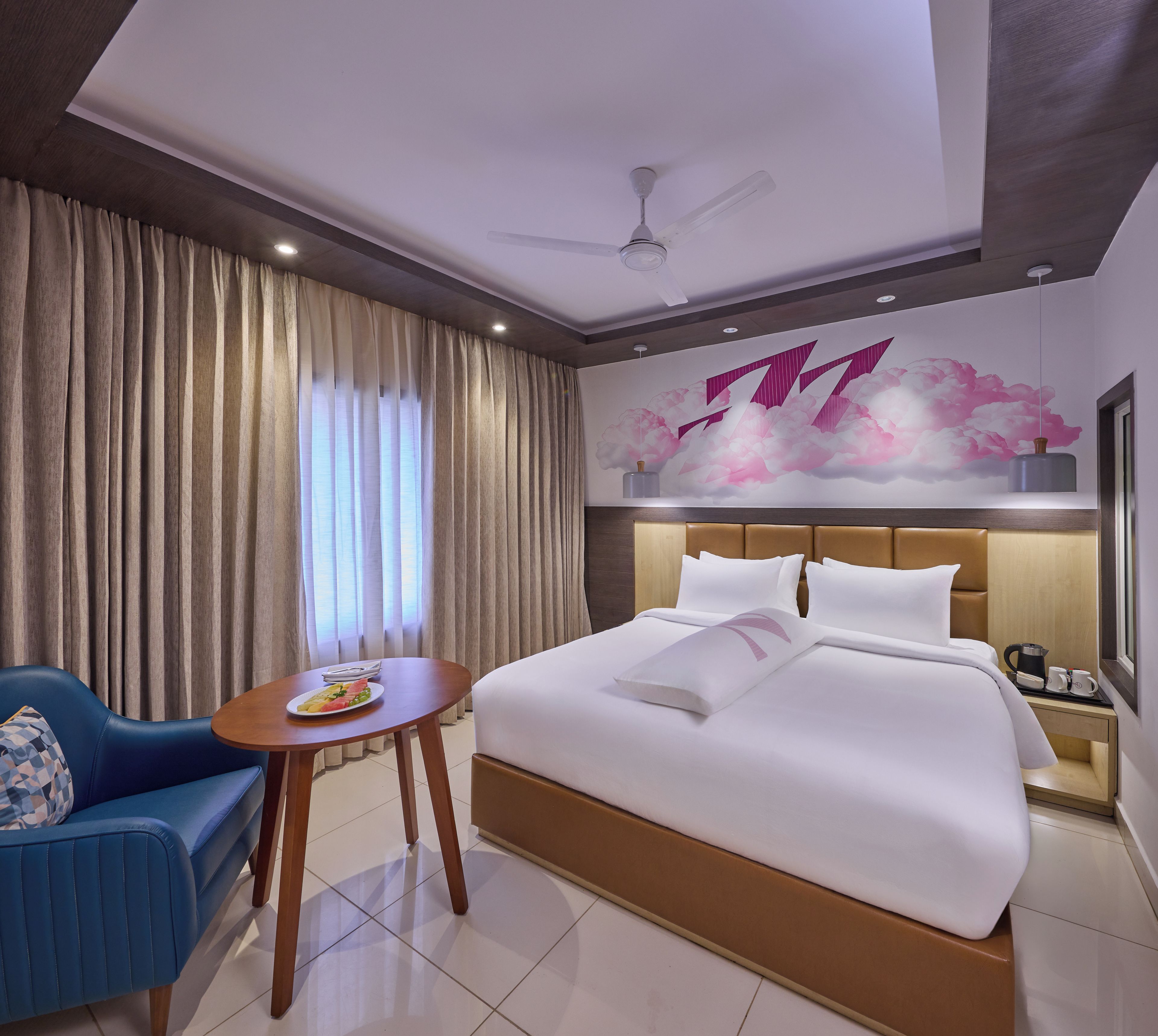 Una habitación de hotel con cama, zona de estar, mesa y una pared decorativa.