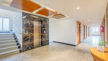 A modern hotel lobby with a marble staircase, elevators, and a long corridor with doors.