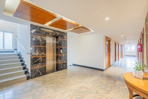 A modern hotel lobby with a marble staircase, elevators, and a long corridor with doors.
