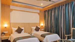 A hotel room with two beds, wooden headboard, a ceiling fan, and a large window with curtains. - Hotel Southern Grand (Vijayawada)