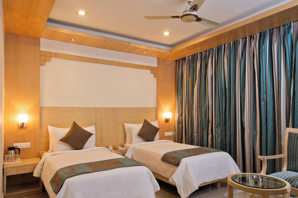 A hotel room with two beds, wooden headboard, a ceiling fan, and a large window with curtains.