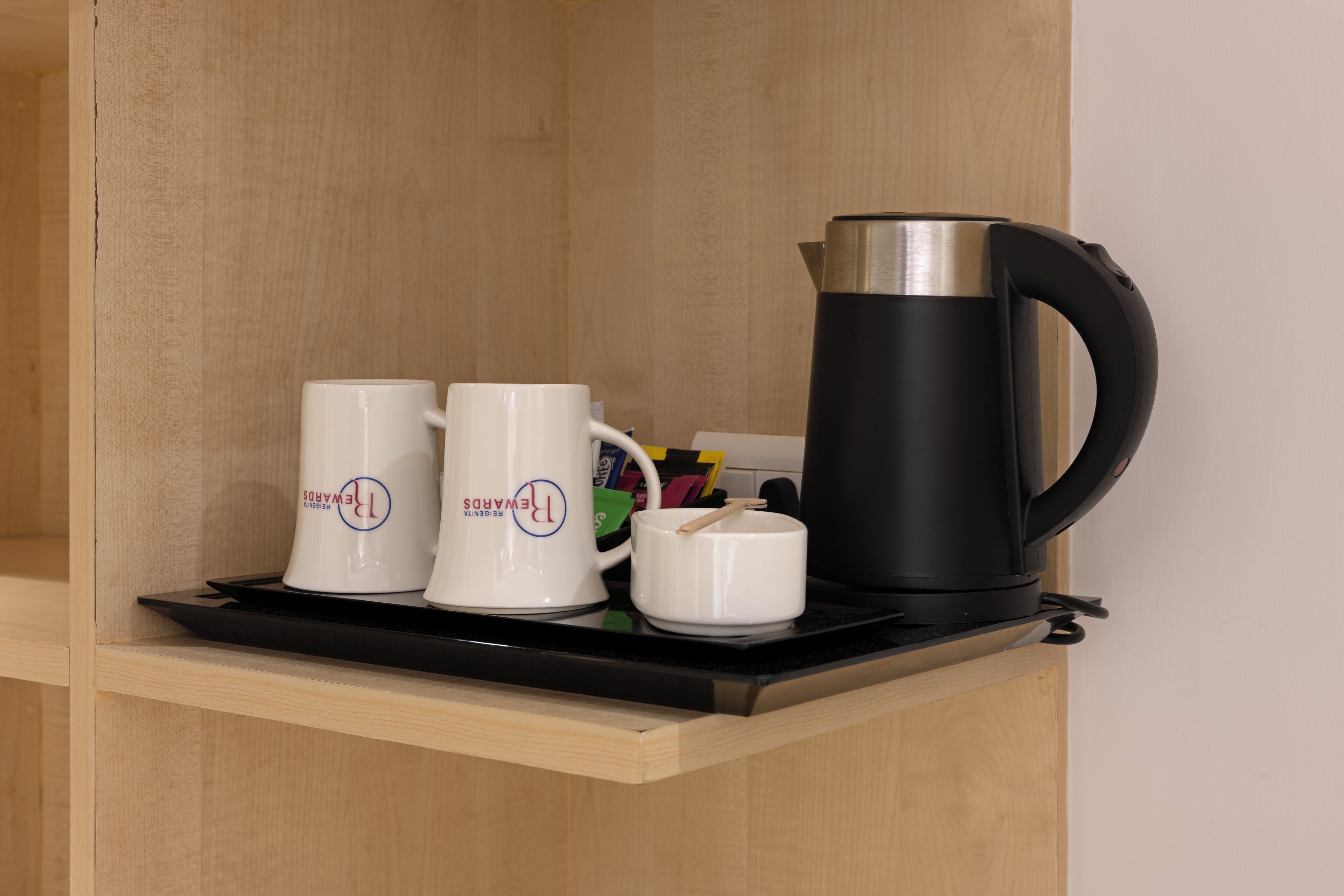 A shelf with a black electric kettle, two white mugs with a logo, and a small white container.