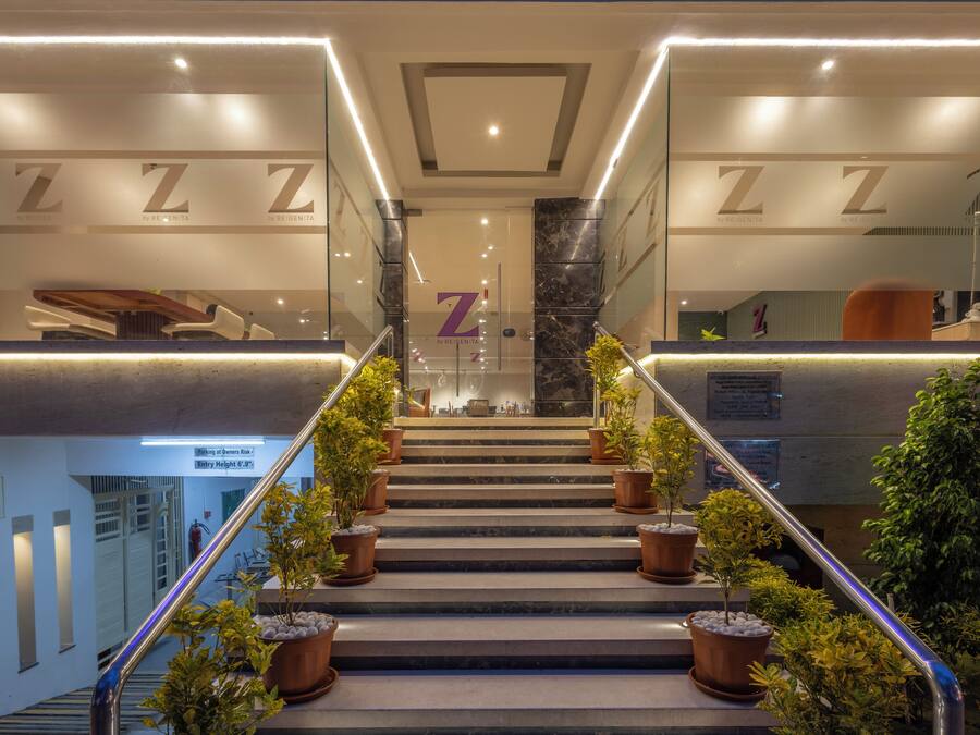 Un intérieur d’hôtel moderne avec un escalier central bordé de rampes de verre, menant à un espace d’accueil signalé par un grand « Z ».