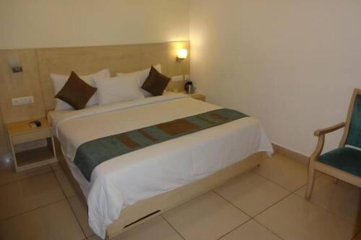 A hotel room with a bed, a nightstand, a chair, and a wall-mounted light.